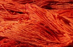 Vibrant strands of fabric dyed with madder root dye powder showcasing deep, earthy red hues.