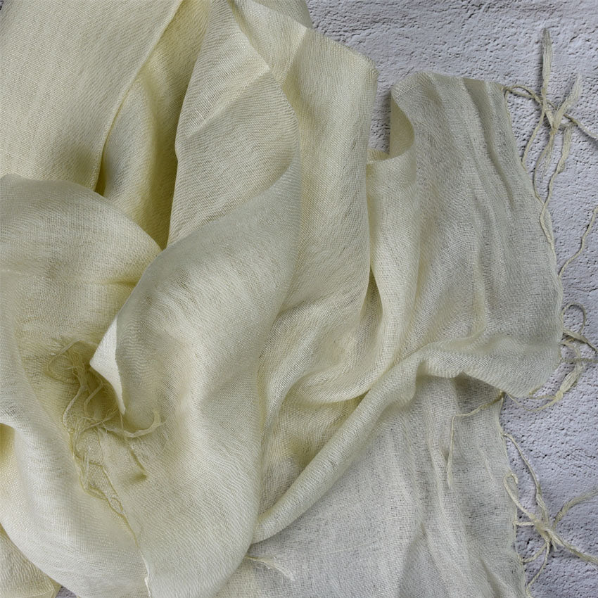 Pale yellow wool silk scarf with tassels draped on textured grey background