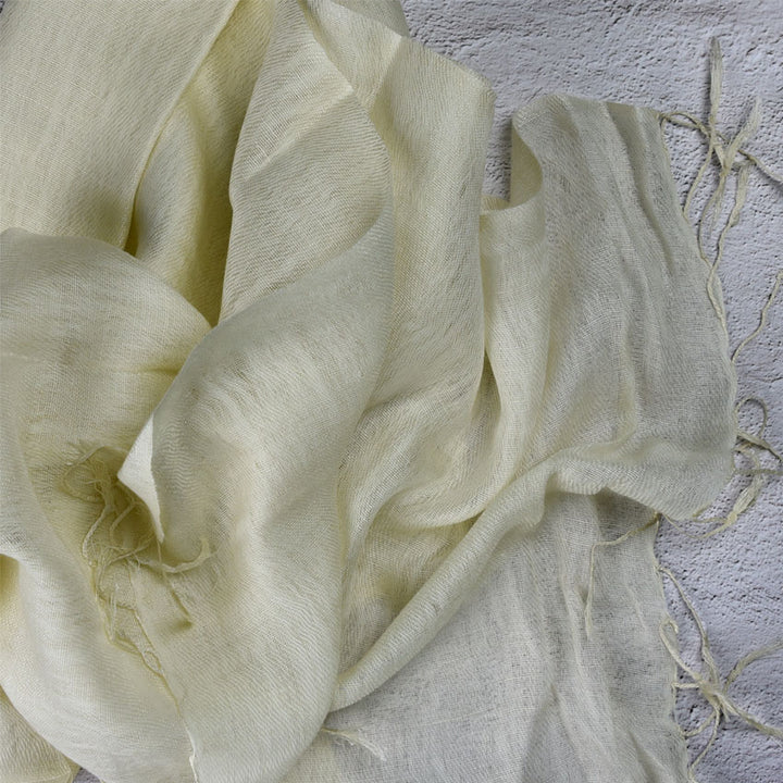 Pale yellow wool silk scarf with tassels draped on textured grey background