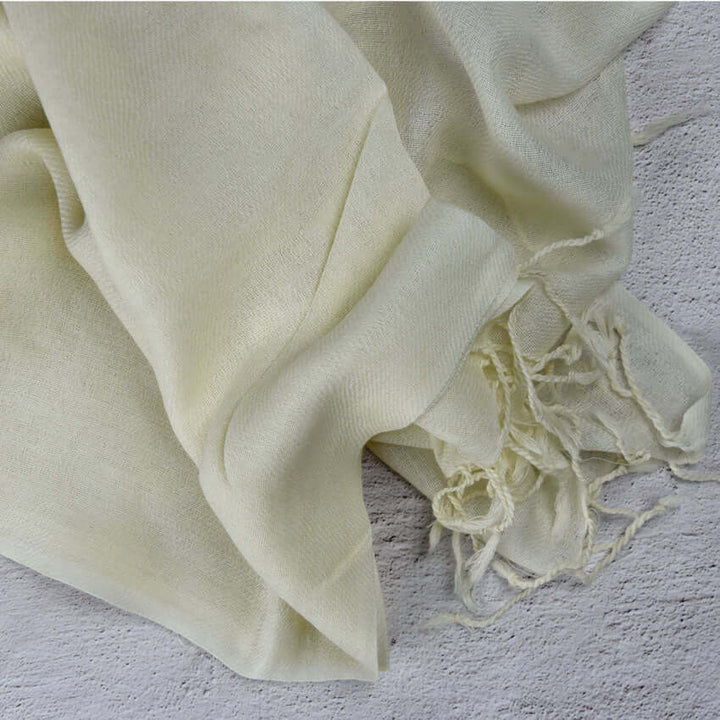 Cream merino wool twill shawl with tassels folded on grey surface