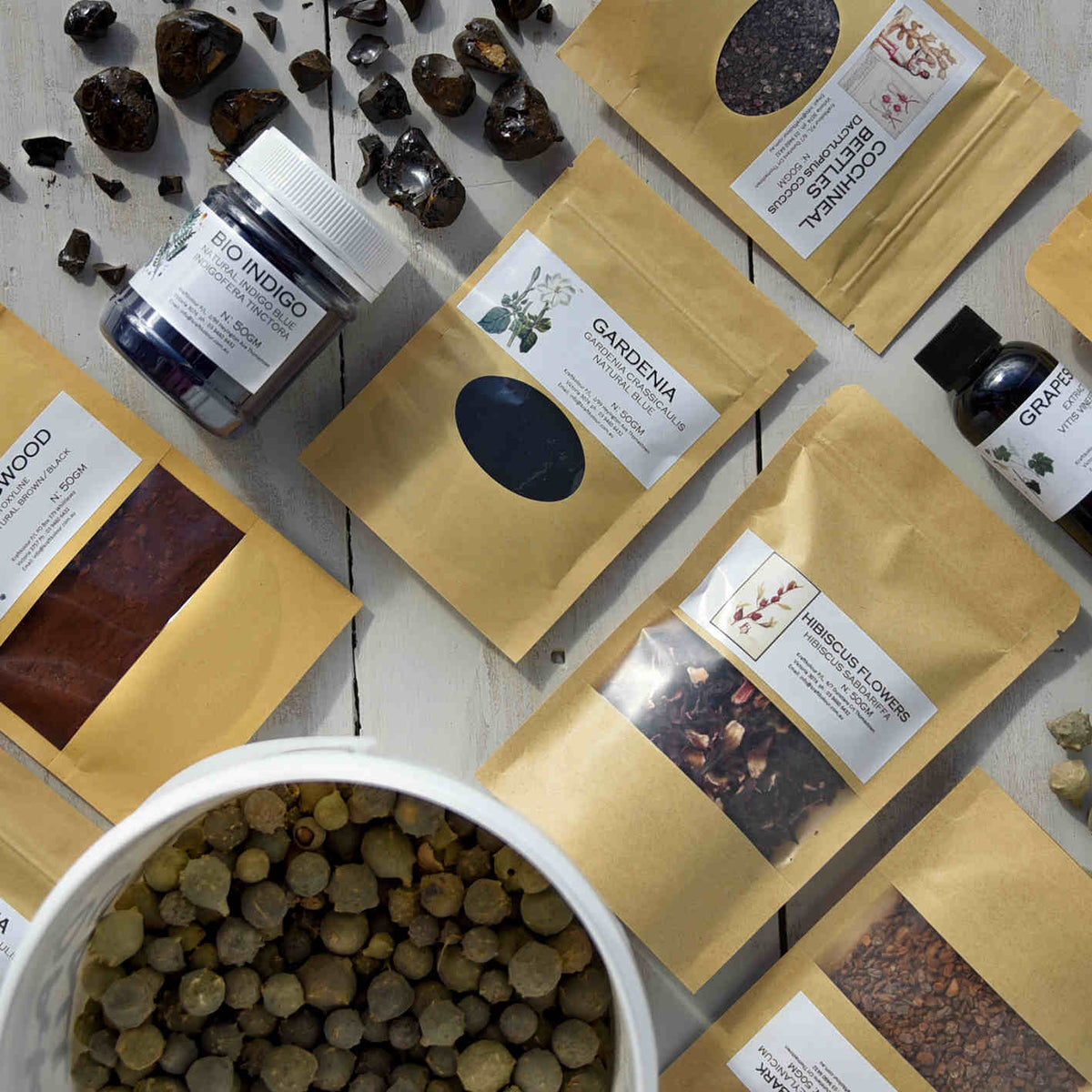 Natural dye powders and botanicals in kraft pouches with indigo jar on wooden table